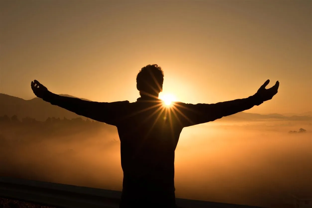 man holding arms out to sunset